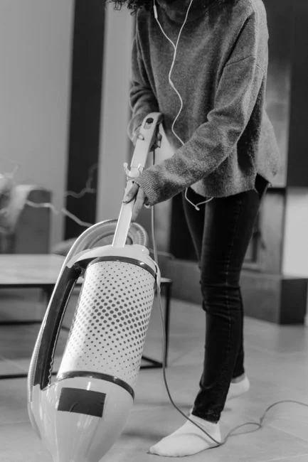 services-01 A professional cleaner in protective gear vacuuming the floor in a modern living room.